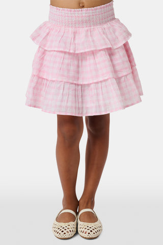 Three girls stand in front of lockers, holding notebooks. Smiling at each other, they are dressed in pink and white outfits, with one wearing the Roller Rabbit Kids Gingham Hearts Sami Skirt. Blue and pink backpacks are visible by the lockers.
