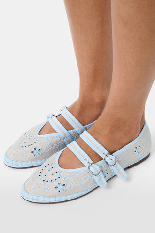 Person holding a pair of gray shoes with decorative elements, wearing a white dress with blue floral patterns.