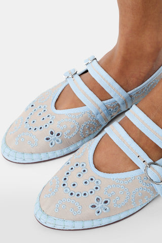 Person holding a pair of gray shoes with decorative elements, wearing a white dress with blue floral patterns.