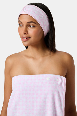 The Roller Rabbit Gingham Hearts Spa Headband is crafted from 100 cotton terrycloth and showcases a pink and white checkered pattern accented with small hearts. It features a convenient hook-and-loop fastener and is displayed laid flat on a white background.