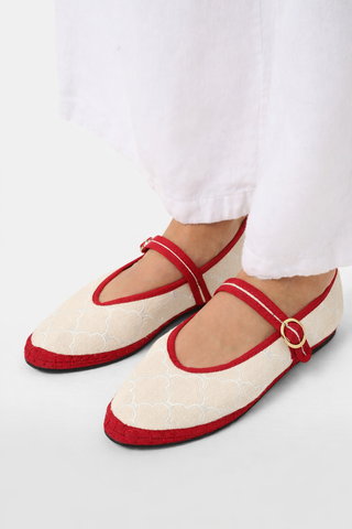 The Jena Embroidery Pierre by FLABELUS is a beige linen Mary Jane shoe with white embroidery, red trim and strap, gold button, and red sole. Made in Spain. Displayed on a plain white background.