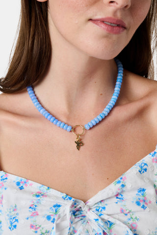 The Beaded Charm Necklace by Roller Rabbit features round, evenly spaced blue beads with a gold clasp, accented by a small gold ring pendant at the center. The necklace is shown against a plain white background.