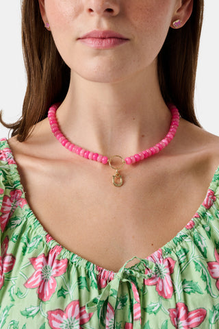 The Beaded Charm Necklace by Roller Rabbit features round pink beads and a small gold ring centerpiece, completed with a gold adjustable clasp and chain. This semi-precious stone necklace is shown against a plain white background.