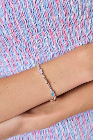 The Icon Party Beaded Bracelet by Roller Rabbit features a beaded silver chain adorned with colorful charms—including a pink monkey, blue elephant, yellow horseshoe, star, moon, and a blue eye—set against a white background.
