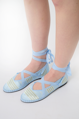 The Positano Stripe Ribbon by FLABELUS is a light blue satin ballet-inspired slipper featuring yellow and white stripes, a pointed toe, blue ankle-wrapping ribbon tie, and a woven sole with visible stitching.