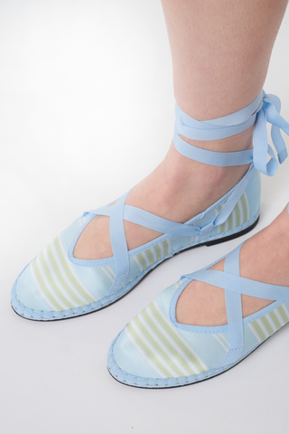 The Positano Stripe Ribbon by FLABELUS is a light blue satin ballet-inspired slipper featuring yellow and white stripes, a pointed toe, blue ankle-wrapping ribbon tie, and a woven sole with visible stitching.