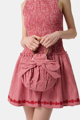 The Roller Rabbit Gingham Miranda Purse features red gingham fabric, a large red and white bow, gathered detailing, and a round bracelet handle, shown against a plain white background.