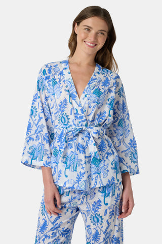 A woman poses barefoot against a plain white background wearing the Roller Rabbit Amanda Christy Set, a matching lounge set with a blue and white floral Amanda print, featuring a belted long-sleeve top and loose-fitting pants.