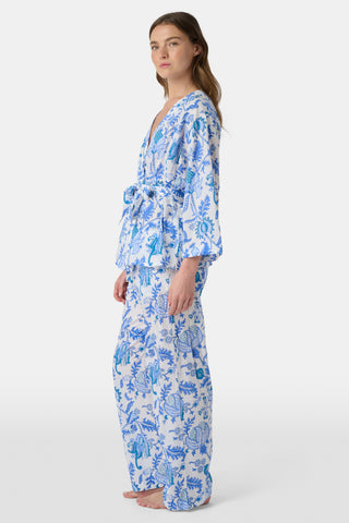 A woman poses barefoot against a plain white background wearing the Roller Rabbit Amanda Christy Set, a matching lounge set with a blue and white floral Amanda print, featuring a belted long-sleeve top and loose-fitting pants.