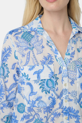 A woman with long blonde hair wears the Roller Rabbit Amanda Guy Shirt, a light blue and white paisley long-sleeve top, paired with white pants, standing against a plain white background.