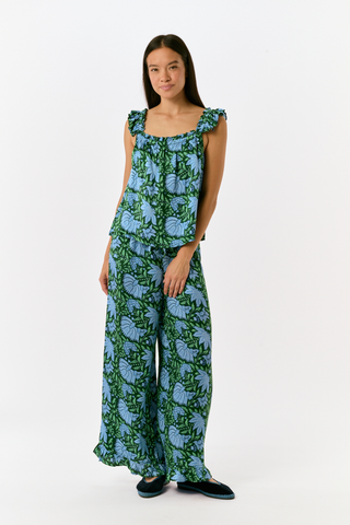 A woman wears the SAPPHIRE Antonia Floral Joanna Set, a washable silk two-piece featuring a green and blue floral print, a sleeveless ruffled-strap top, and wide-leg trousers.