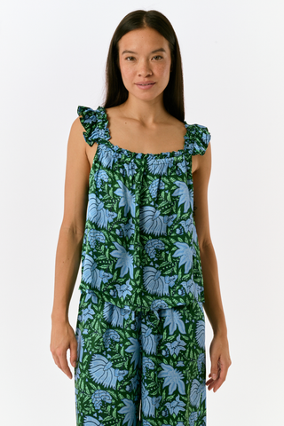 A woman wears the SAPPHIRE Antonia Floral Joanna Set, a washable silk two-piece featuring a green and blue floral print, a sleeveless ruffled-strap top, and wide-leg trousers.