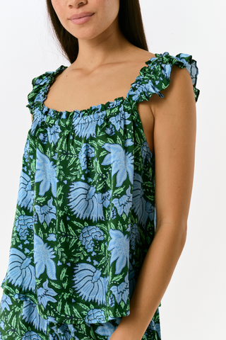 A woman wears the SAPPHIRE Antonia Floral Joanna Set, a washable silk two-piece featuring a green and blue floral print, a sleeveless ruffled-strap top, and wide-leg trousers.