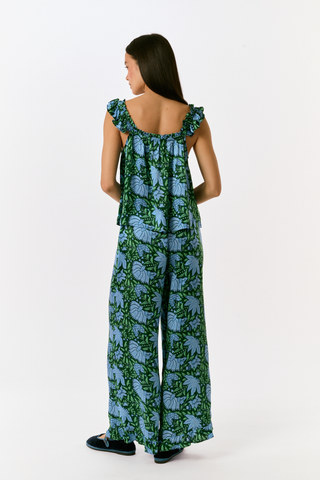 A woman wears the SAPPHIRE Antonia Floral Joanna Set, a washable silk two-piece featuring a green and blue floral print, a sleeveless ruffled-strap top, and wide-leg trousers.