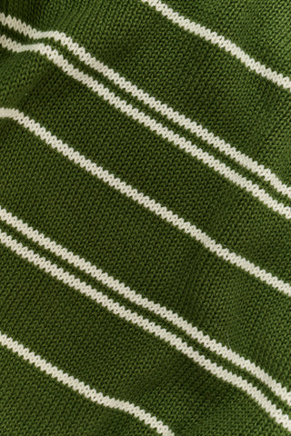 A person wearing the Roller Rabbit Autumn Stripe Olivia Pant—green and white striped, pull-on, flared—and a matching sweater lifts the hem to reveal their midriff. Brown slippers are visible. The background is white.