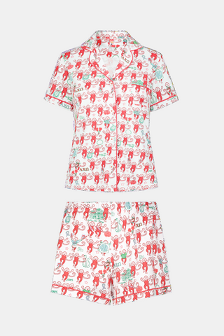 Wearing Roller Rabbit’s Alpha Chi Omega Monkey Polo Pajamas in a playful print, a woman leans against a brick wall, smiling softly as she holds two pink and white patterned notebooks and an iced coffee with a straw.