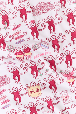 The Roller Rabbit Alpha Phi Monkey Polo Pajamas are a two-piece set crafted from soft Pima Cotton, featuring a white base adorned with playful red cartoon monkey prints and whimsical text. The short-sleeve top includes a front button placket, while the matching shorts feature an elastic waistband, all displayed on a plain background.