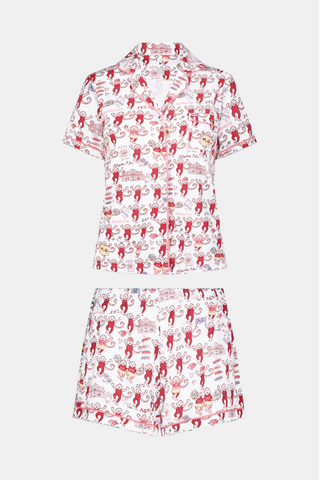 The Roller Rabbit Alpha Phi Monkey Polo Pajamas are a two-piece set crafted from soft Pima Cotton, featuring a white base adorned with playful red cartoon monkey prints and whimsical text. The short-sleeve top includes a front button placket, while the matching shorts feature an elastic waistband, all displayed on a plain background.