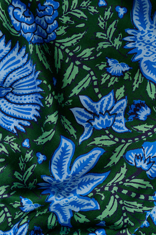A woman wears the SAPPHIRE Antonia Floral Joanna Set, a washable silk two-piece featuring a green and blue floral print, a sleeveless ruffled-strap top, and wide-leg trousers.