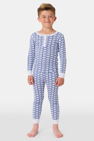 A girl wears Kids Hathi Pajamas—blue and white, full-length, long-sleeve onesie with a white elephant print and white cuffs, crafted from 100% Pima Cotton—smiling barefoot against a plain light background.