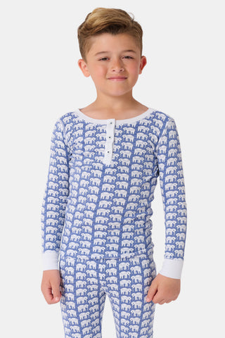 A girl wears Kids Hathi Pajamas—blue and white, full-length, long-sleeve onesie with a white elephant print and white cuffs, crafted from 100% Pima Cotton—smiling barefoot against a plain light background.