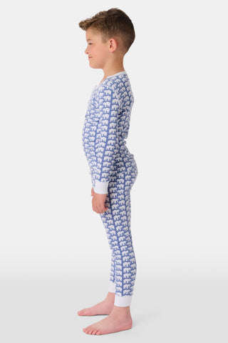 A girl wears Kids Hathi Pajamas—blue and white, full-length, long-sleeve onesie with a white elephant print and white cuffs, crafted from 100% Pima Cotton—smiling barefoot against a plain light background.