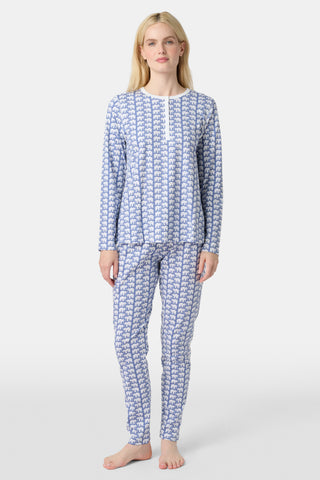 A woman stands barefoot in Roller Rabbit's Hathi Pajamas, a blue and white cotton set with a repeating elephant print, featuring a long-sleeve top and pants, against a plain white background.