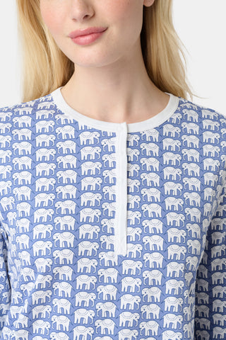 A woman stands barefoot in Roller Rabbit's Hathi Pajamas, a blue and white cotton set with a repeating elephant print, featuring a long-sleeve top and pants, against a plain white background.