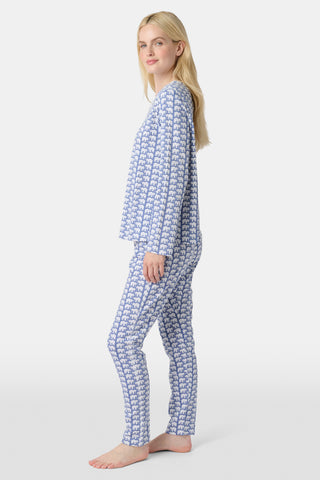 A woman stands barefoot in Roller Rabbit's Hathi Pajamas, a blue and white cotton set with a repeating elephant print, featuring a long-sleeve top and pants, against a plain white background.