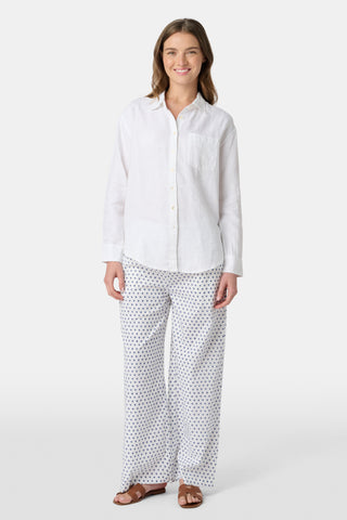 A woman wears the Roller Rabbit Boyfriend Shirt, a menswear-inspired white button-up with a chest pocket, paired with loose white pants featuring a navy polka dot pattern, standing against a plain light background.