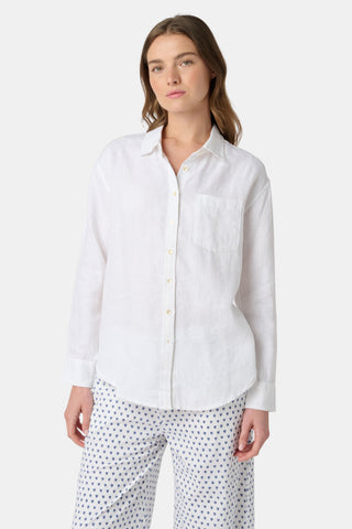 A woman stands against a plain background wearing the Roller Rabbit Boyfriend Shirt, a white linen menswear-inspired top with a chest pocket, paired with loose white pants featuring small blue polka dots.