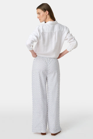 A person stands facing forward, wearing Roller Rabbit’s Hearts Kaylee Pant and a white cotton button-up shirt with brown flat sandals against a plain light background.