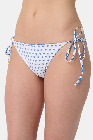 A person wears Roller Rabbit's Monkey/Hearts Serena Bikini Bottom in blue and white with monkey print and side ties. Only the torso and upper legs are visible against a plain background. This reversible bikini bottom provides UPF 50+ sun protection.