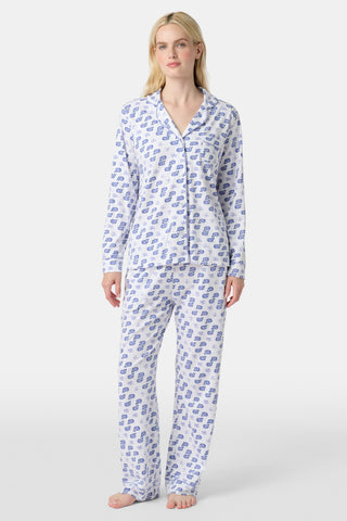 A woman stands barefoot in the Roller Rabbit Moby Long Sleeve Polo Pajamas, featuring a blue geometric-patterned white top and pants. Made from soft pima cotton, the comfy set is shown against a plain white background.
