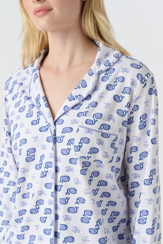 A woman stands barefoot in the Roller Rabbit Moby Long Sleeve Polo Pajamas, featuring a blue geometric-patterned white top and pants. Made from soft pima cotton, the comfy set is shown against a plain white background.