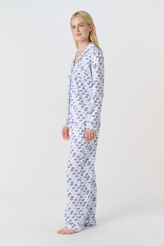 A woman stands barefoot in the Roller Rabbit Moby Long Sleeve Polo Pajamas, featuring a blue geometric-patterned white top and pants. Made from soft pima cotton, the comfy set is shown against a plain white background.
