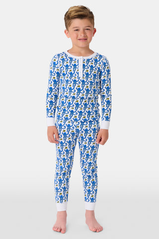 A young girl with curly hair stands barefoot in Kids Monkey Pajamas—a matching long-sleeve top and pants set made from soft 100% cotton, featuring playful monkey prints, against a plain white background.