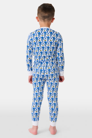 A young girl with curly hair stands barefoot in Kids Monkey Pajamas—a matching long-sleeve top and pants set made from soft 100% cotton, featuring playful monkey prints, against a plain white background.