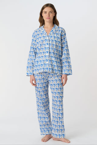 A woman smiles in the Monkey Loungewear long sleeve pajama set by Roller Rabbit, featuring a blue and white floral pattern. She stands barefoot with hands on hips against a plain white background.