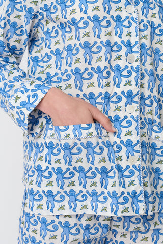 A woman smiles in the Monkey Loungewear long sleeve pajama set by Roller Rabbit, featuring a blue and white floral pattern. She stands barefoot with hands on hips against a plain white background.