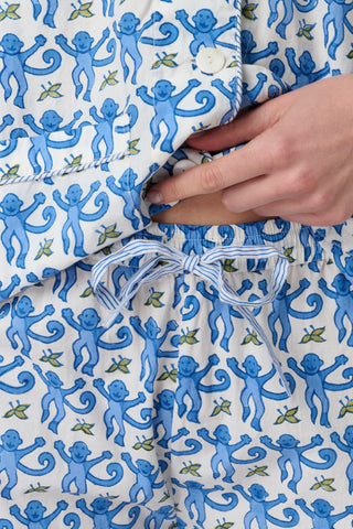 A woman smiles in the Monkey Loungewear long sleeve pajama set by Roller Rabbit, featuring a blue and white floral pattern. She stands barefoot with hands on hips against a plain white background.