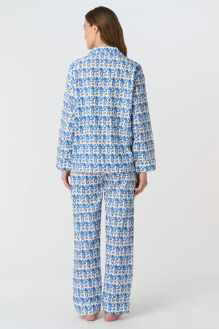 A woman smiles in the Monkey Loungewear long sleeve pajama set by Roller Rabbit, featuring a blue and white floral pattern. She stands barefoot with hands on hips against a plain white background.