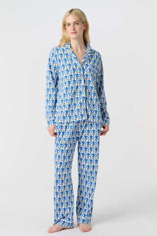 A person with long blonde hair wears Roller Rabbit Monkey Long Sleeve Polo Pajamas in blue and white Pima cotton, standing barefoot on a white background.
