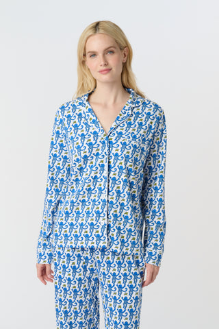 A person with long blonde hair wears Roller Rabbit Monkey Long Sleeve Polo Pajamas in blue and white Pima cotton, standing barefoot on a white background.