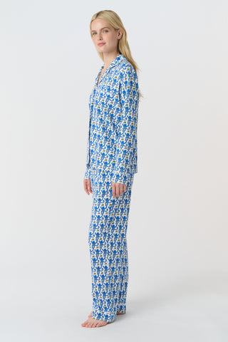 A person with long blonde hair wears Roller Rabbit Monkey Long Sleeve Polo Pajamas in blue and white Pima cotton, standing barefoot on a white background.