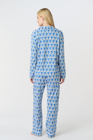 A person with long blonde hair wears Roller Rabbit Monkey Long Sleeve Polo Pajamas in blue and white Pima cotton, standing barefoot on a white background.