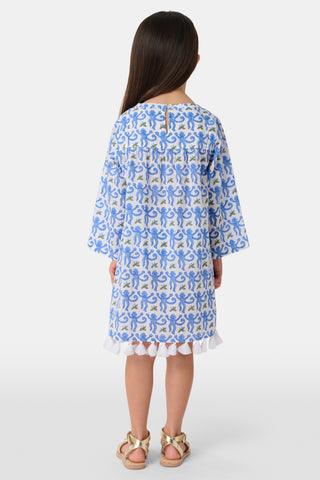 A young girl with long dark hair wears a Roller Rabbit Kids Monkey Serafina Tunic, a blue-and-white cotton voile dress with long sleeves and white fringe at the hem, standing against a plain white background.