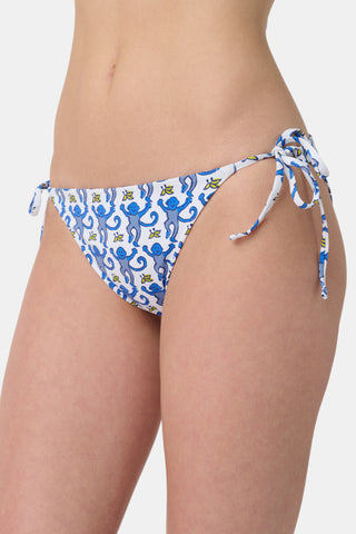 A person wears Roller Rabbit's Monkey/Hearts Serena Bikini Bottom in blue and white with monkey print and side ties. Only the torso and upper legs are visible against a plain background. This reversible bikini bottom provides UPF 50+ sun protection.