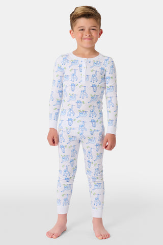 A young boy stands barefoot, smiling and facing forward in Roller Rabbit's Kids Sleepy Sloth Pajamas—a white, long-sleeve cotton PJ set with playful blue and green sloth prints—against a plain white background.