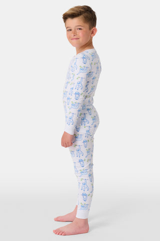 A young boy stands barefoot, smiling and facing forward in Roller Rabbit's Kids Sleepy Sloth Pajamas—a white, long-sleeve cotton PJ set with playful blue and green sloth prints—against a plain white background.